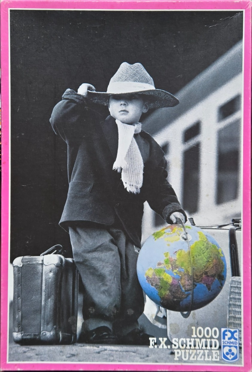 A black and white photograph of a young boy in a hat holding a colorful globe and standing by a suitcase.
