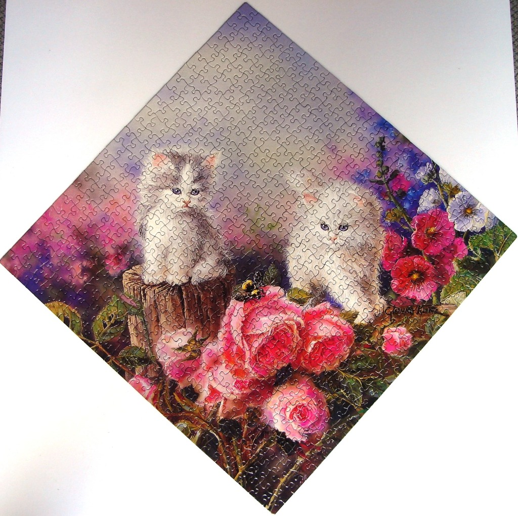 Two fluffy kittens sit among vibrant pink roses and hollyhocks in a dreamlike garden setting.
