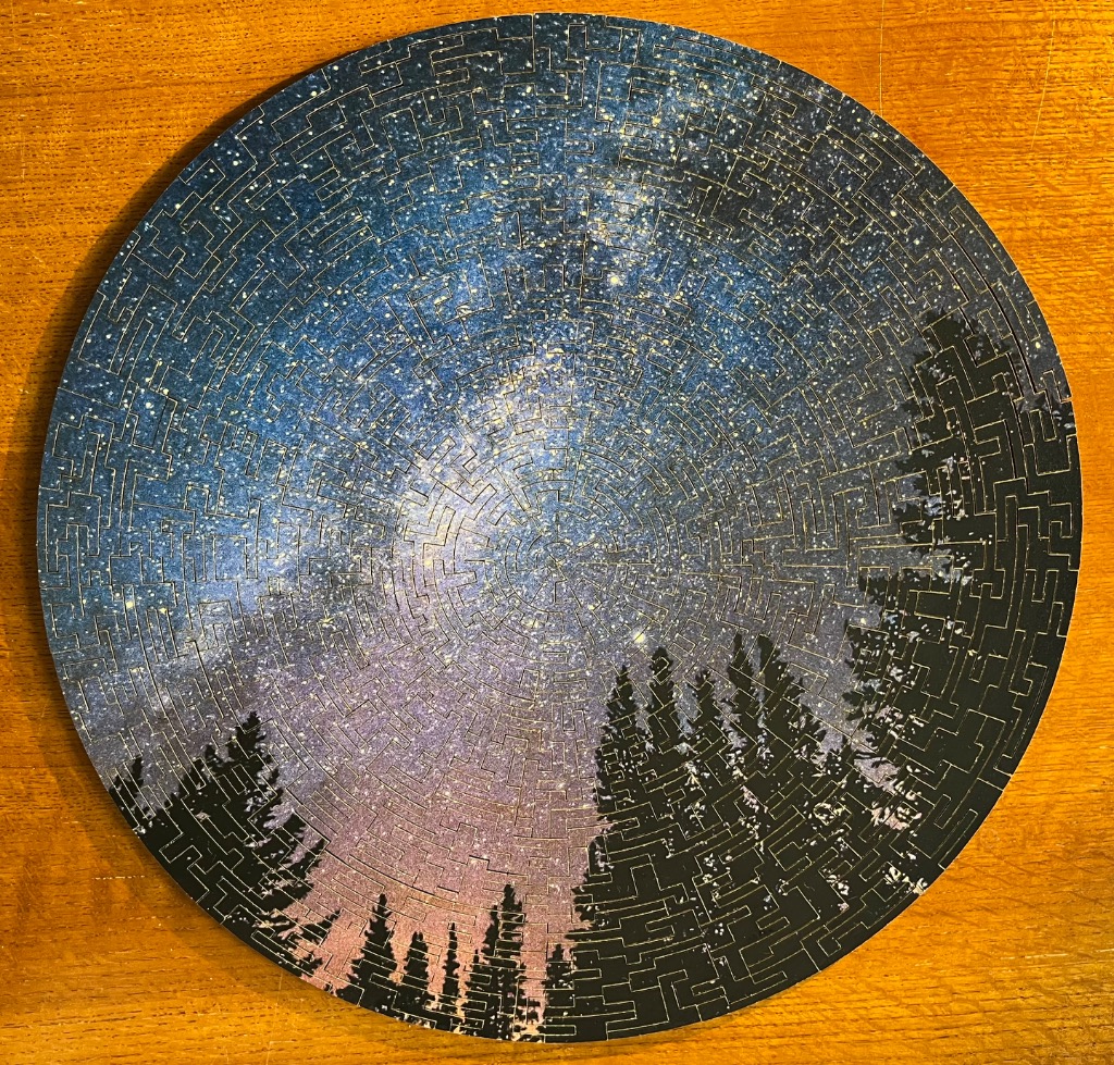 A circular image showing a starry night sky above a silhouetted forest canopy.