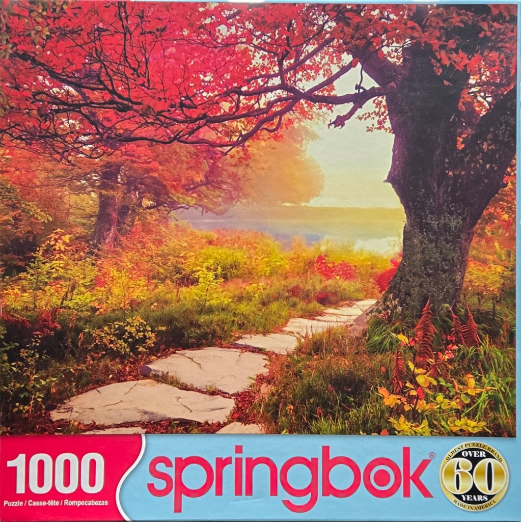 A stone path winds through a vibrant autumn forest with red leaves and a distant sunlit meadow.
