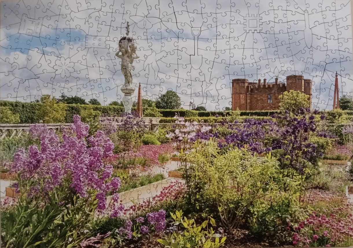 A lush ornamental garden featuring purple flowers and a stone statue with a distant brick castle in the background.
