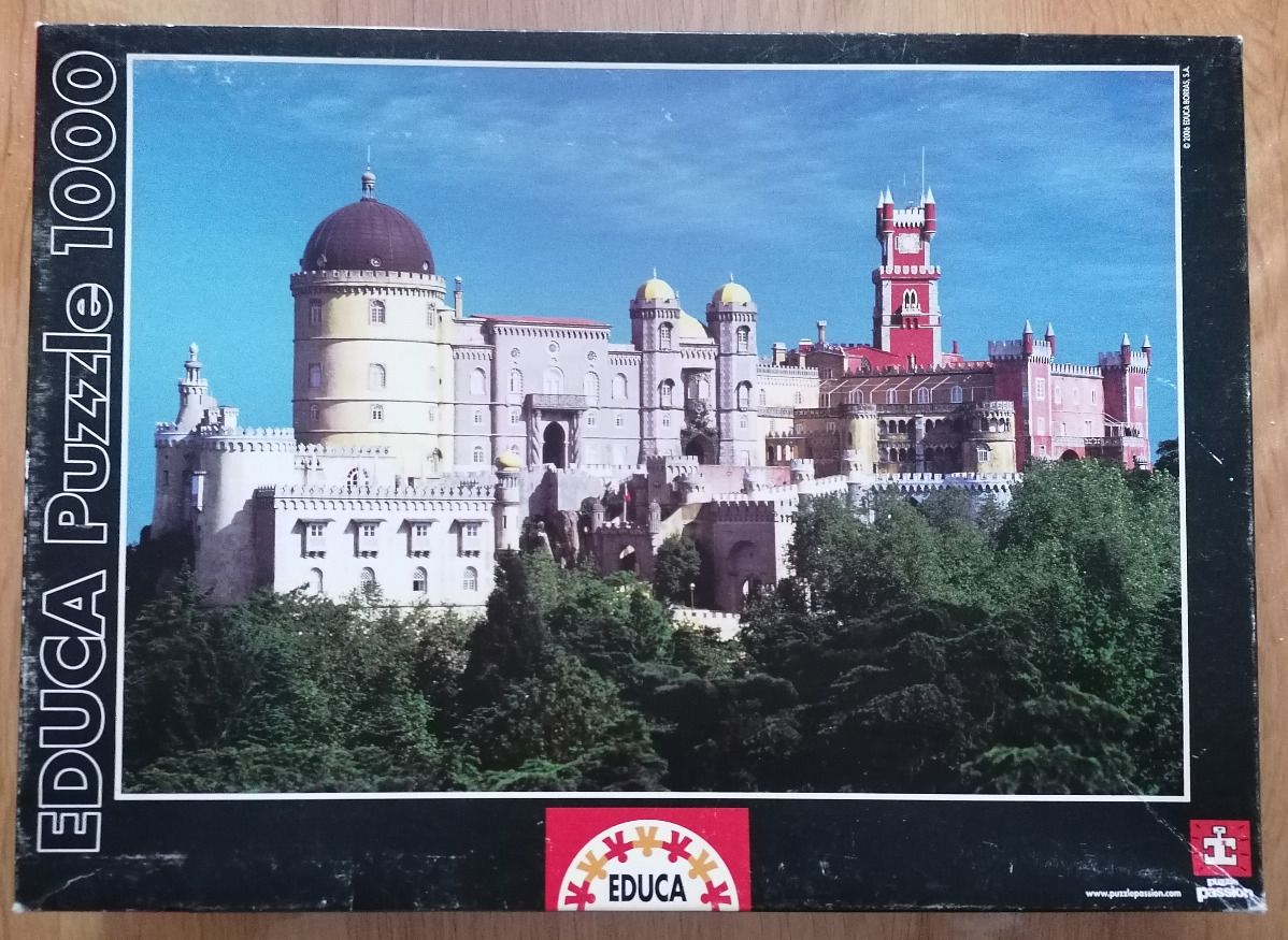 A clear, sunny-day photograph of the colorful Pena Palace in Sintra, Portugal, set against a bright blue sky.