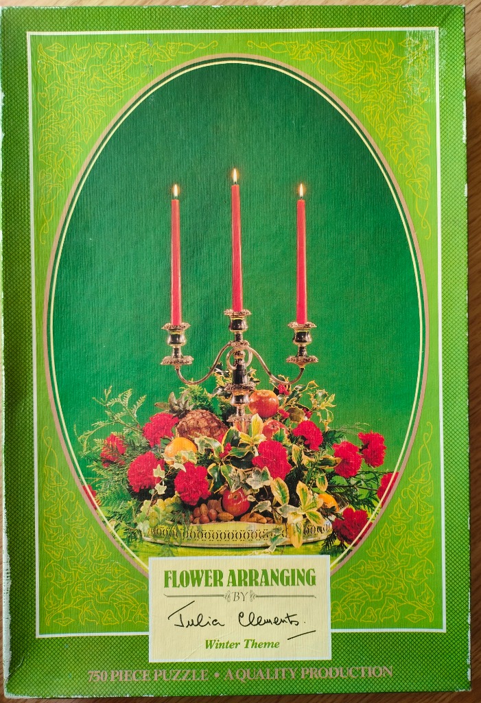 A silver candelabra with three lit red candles surrounded by a festive floral arrangement against a green background.
