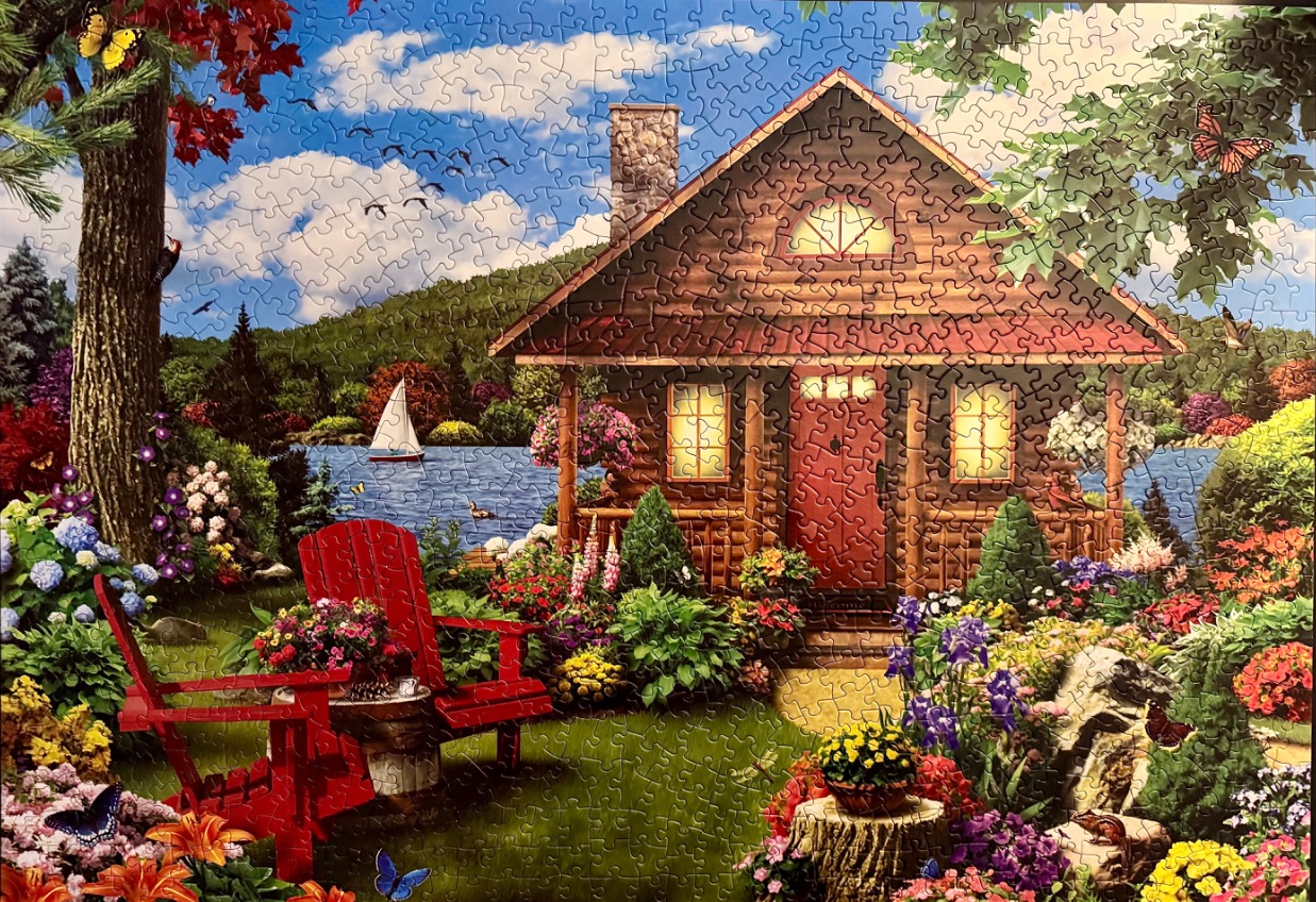 A cozy log cabin beside a blue lake with a vibrant garden in the foreground.