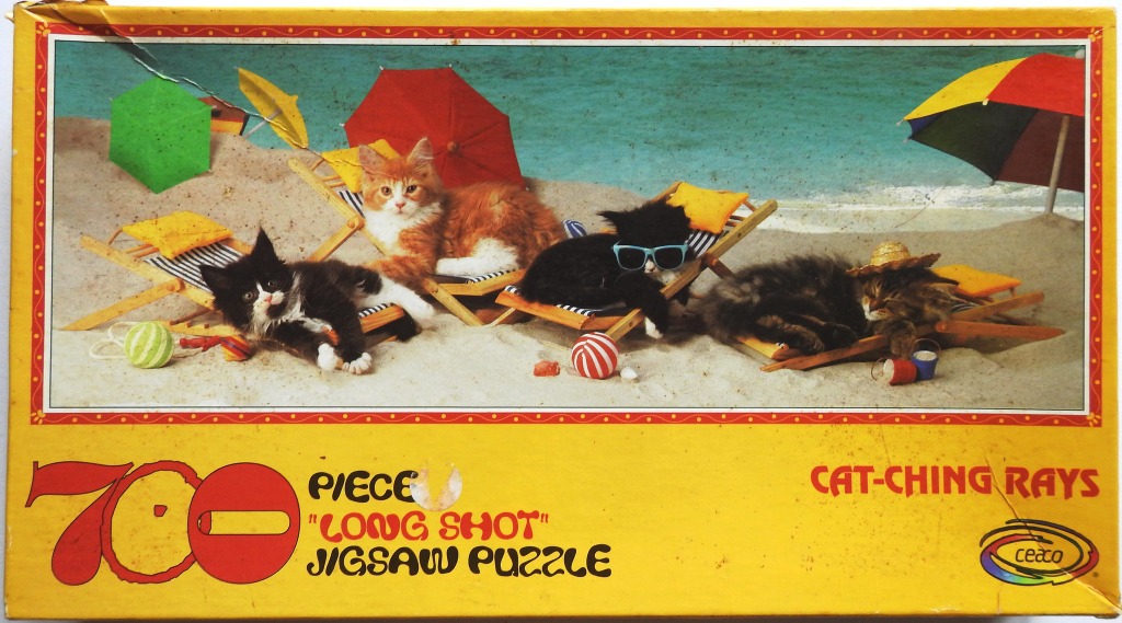 Four kittens relaxing on wooden lounge chairs on a sandy beach under colorful umbrellas.