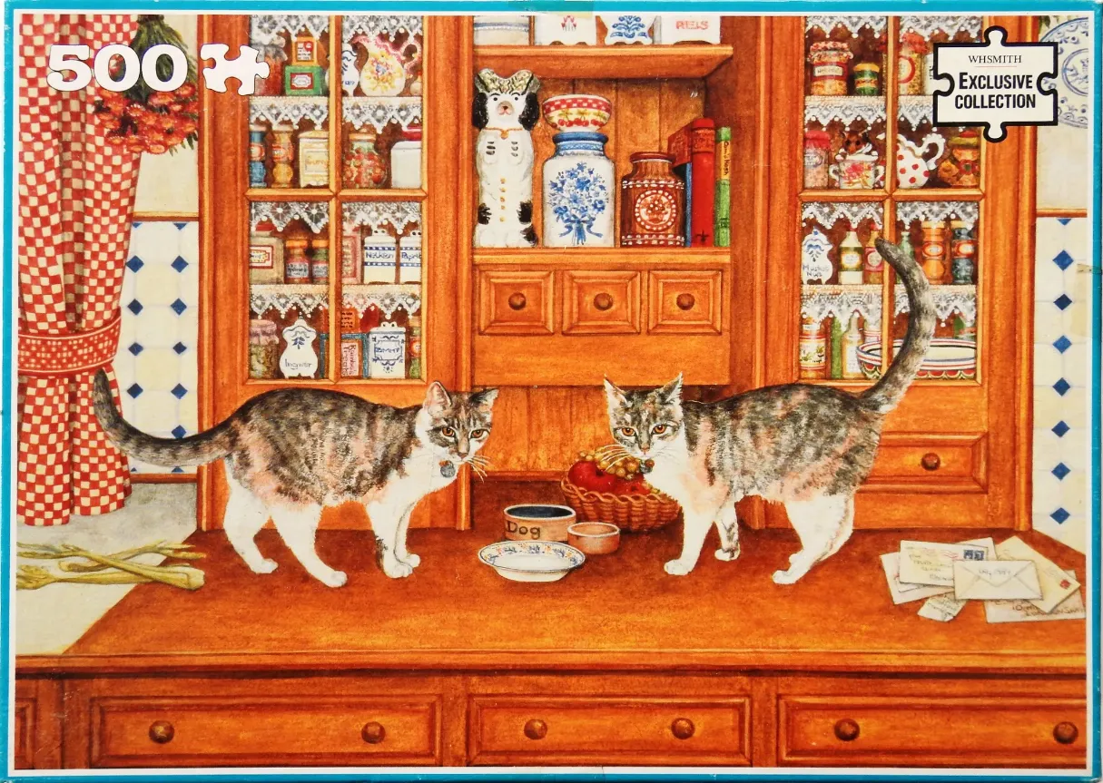 Two tabby cats stand on a wooden kitchen counter in front of a hutch filled with jars and decorations.