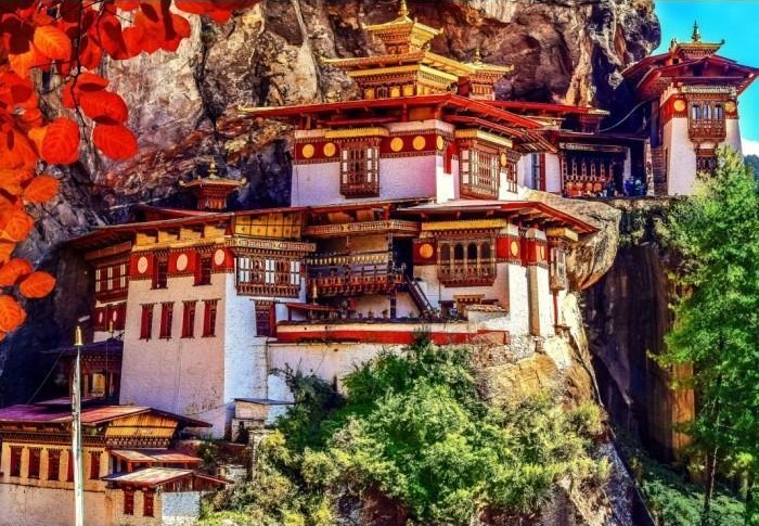 Taktsang Monastery perched precariously on a sheer Himalayan cliff face surrounded by autumnal foliage.