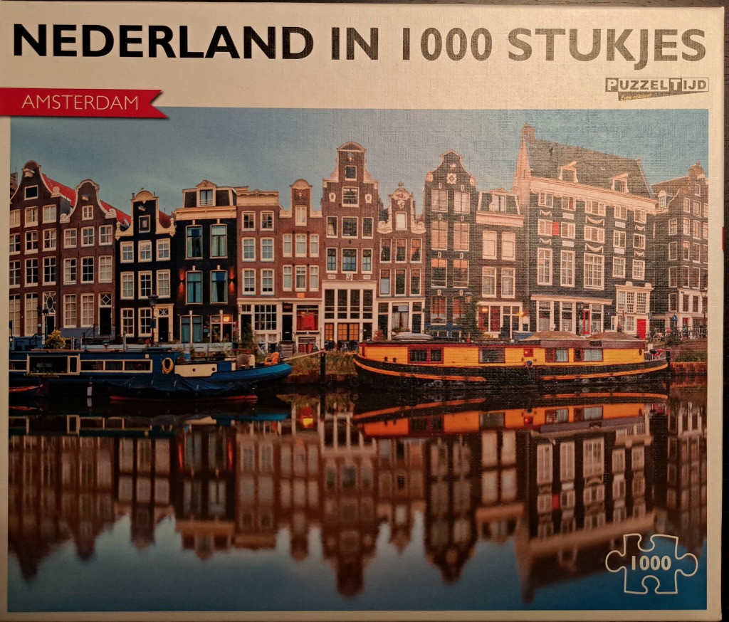 A row of historic canal houses in Amsterdam reflected in still water with two houseboats in the foreground.