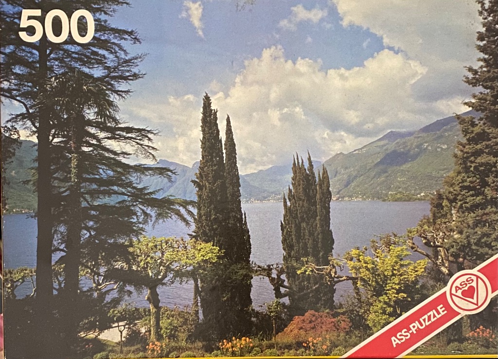 A serene lakeside view with tall cypress trees, calm water, and distant mountains under a cloudy sky.