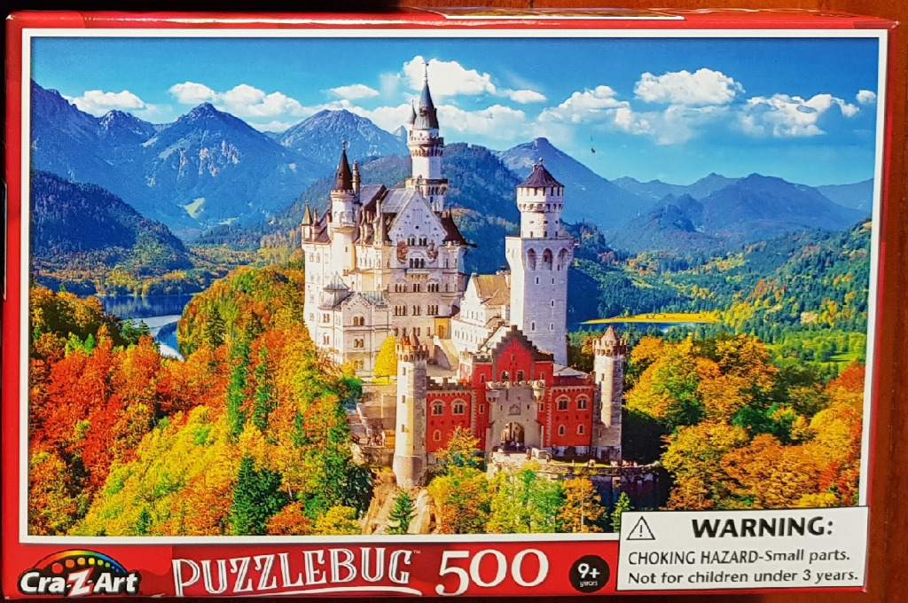 A fairytale castle nestled in a vibrant autumn forest with mountains in the background under a blue sky.