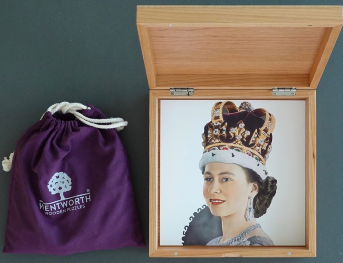A portrait of Queen Elizabeth II wearing the Imperial State Crown inside a wooden case next to a purple drawstring bag.