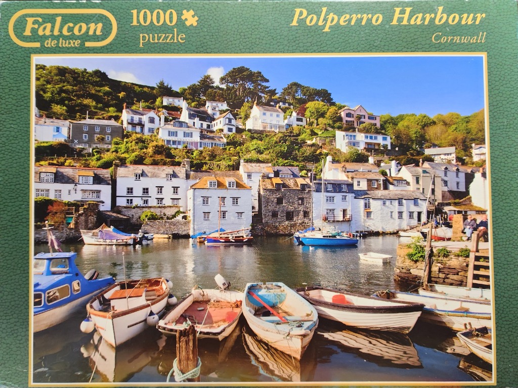 A sunny, scenic view of Polperro Harbour in Cornwall with colorful fishing boats moored in the foreground.