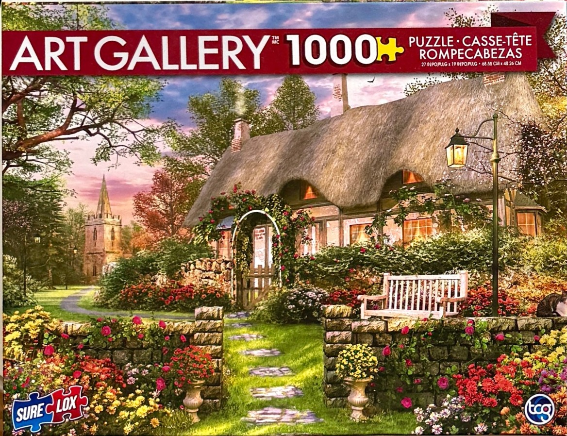 A thatched cottage with a blooming rose garden at sunset and a stone church steeple in the distance.