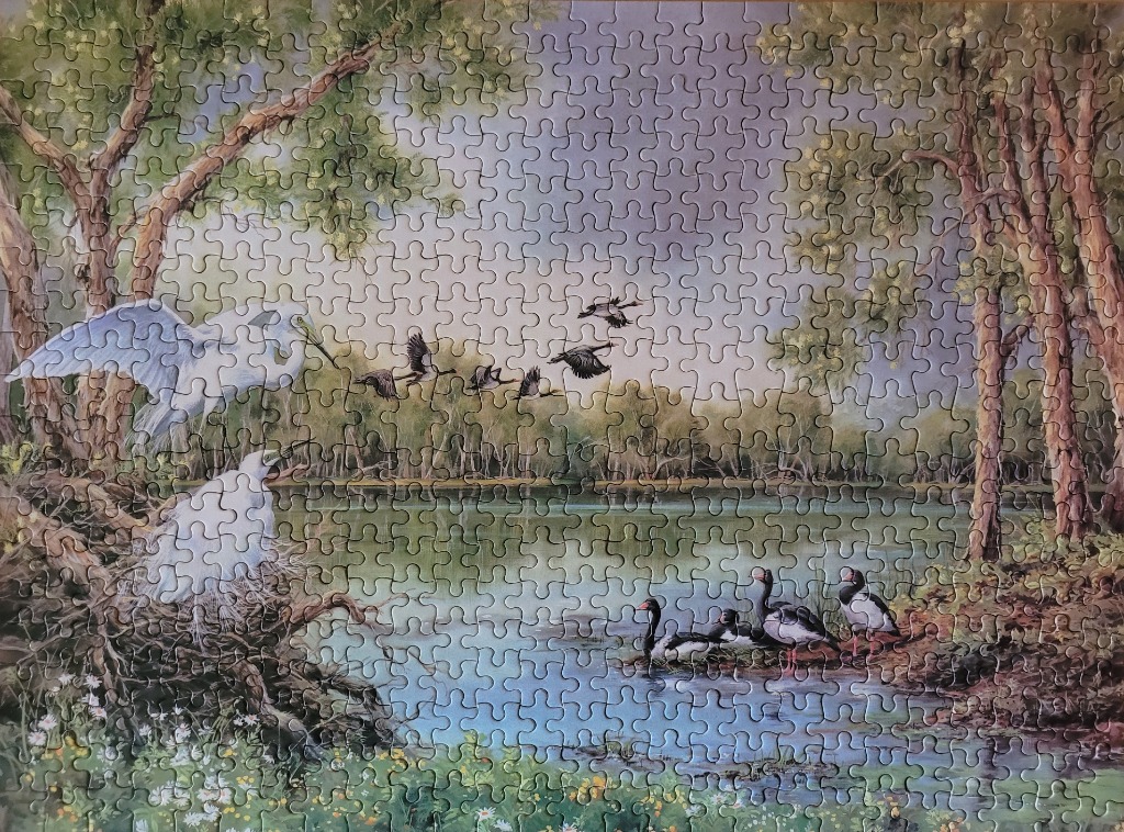 A peaceful lakeside scene with white egrets nesting and black and white water birds wading in the shallows.