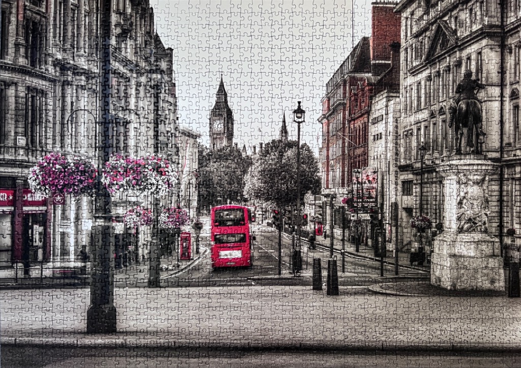 A black and white London street scene with a vibrant red double-decker bus and pink hanging flowers.