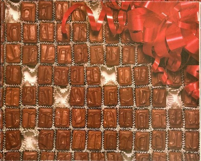 A close-up view of a box of assorted chocolates decorated with a large, bright red ribbon and bow.