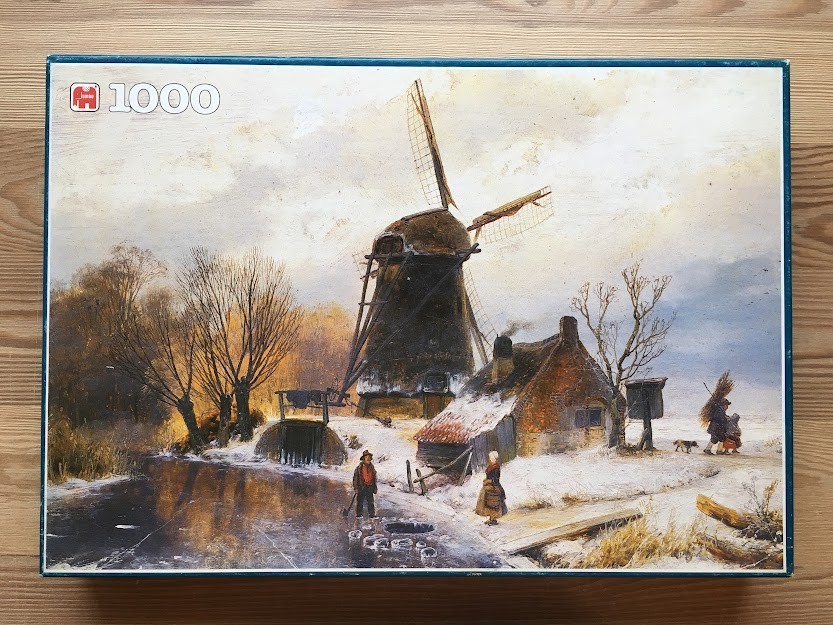 A wintry Dutch landscape featuring a dark windmill, a small cottage, and figures on a frozen canal.