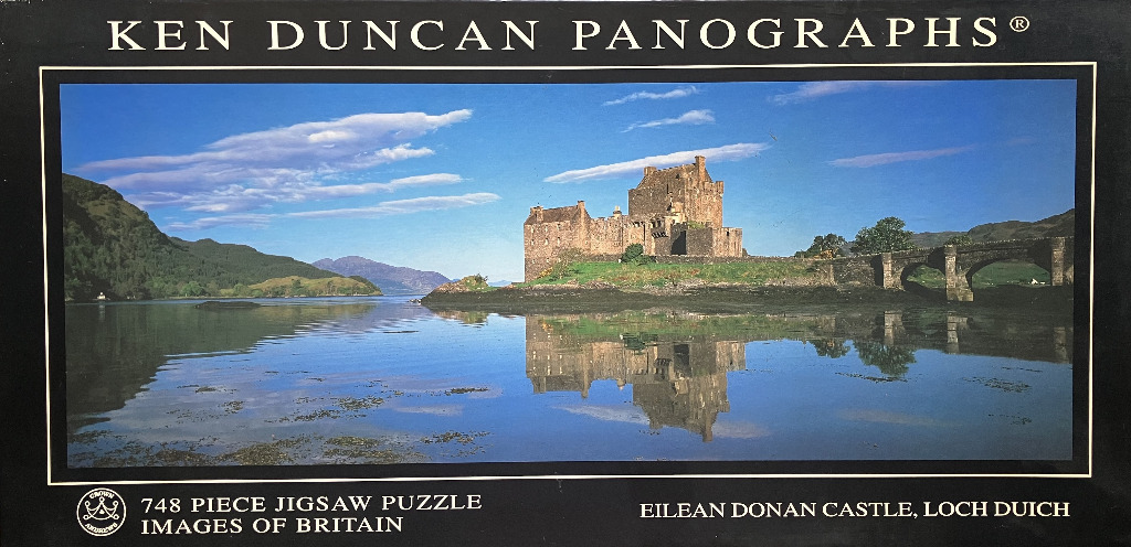 A panoramic photograph of Eilean Donan Castle reflected in the calm waters of Loch Duich under a clear blue sky.