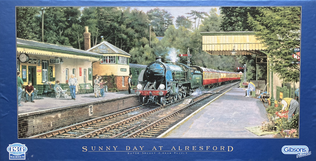 Steam train arriving at a sunny British railway station platform with passengers and greenery.