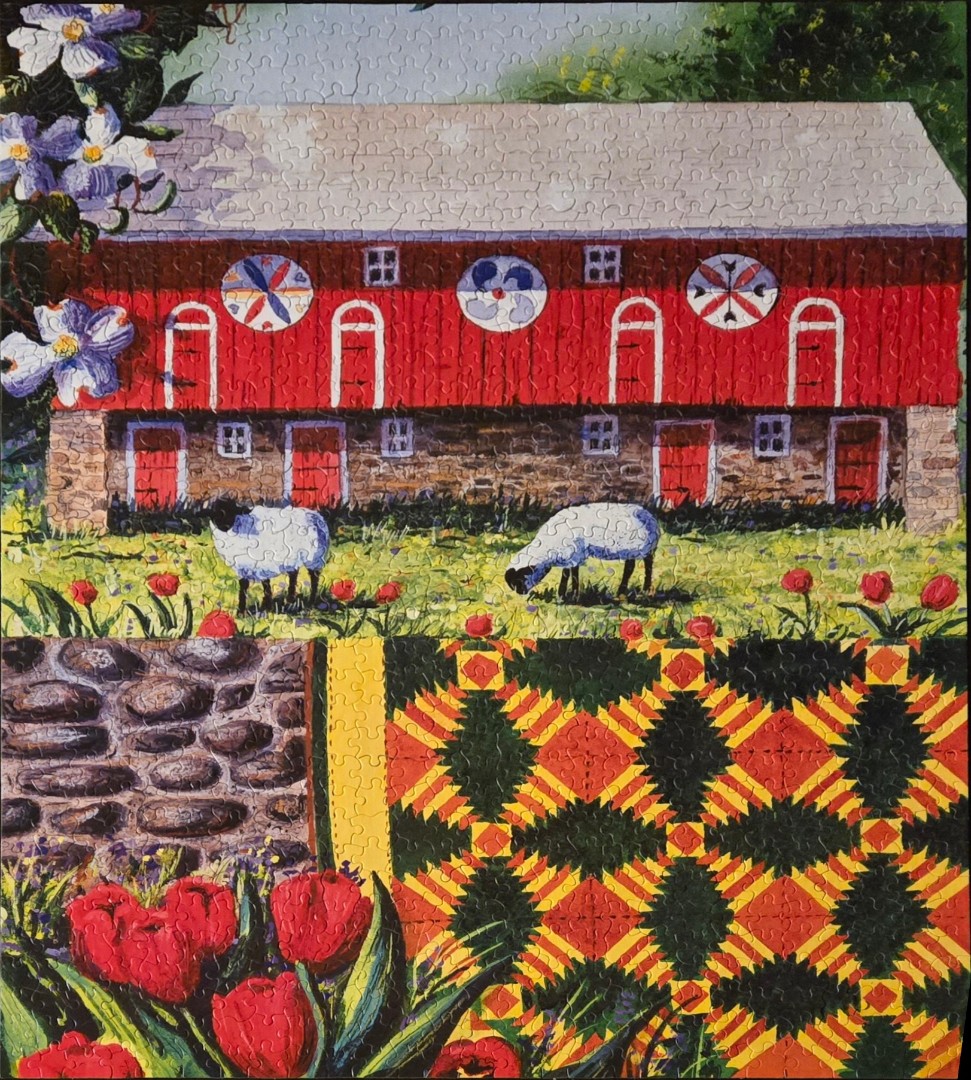 A red barn with circular quilt patterns, grazing sheep, and foreground tulips and a quilted blanket.