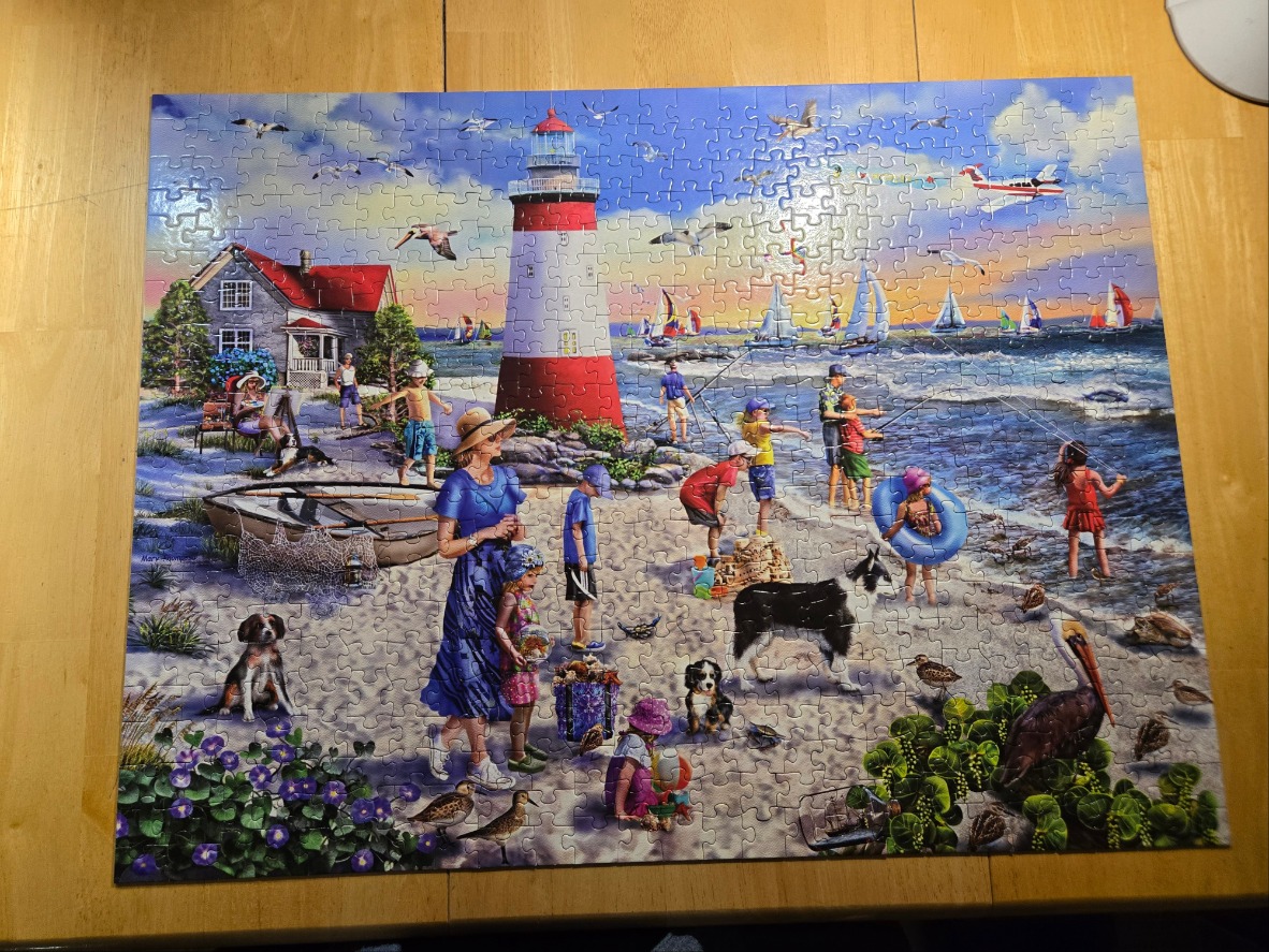 A lively beach scene featuring a red and white lighthouse, a cottage, and many people and dogs.