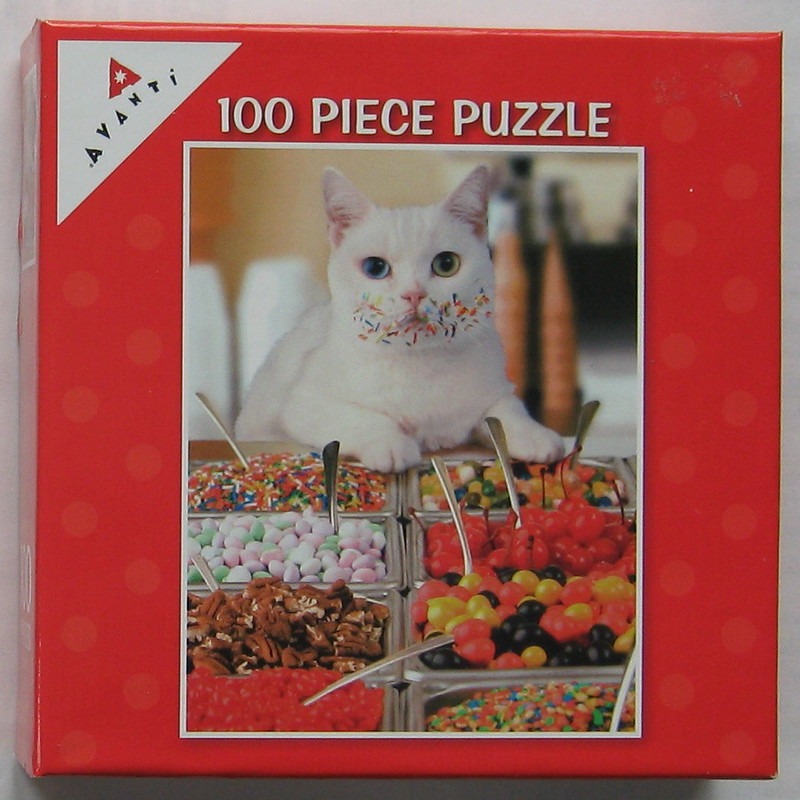 White cat with colorful sprinkles on its face sitting behind an ice cream topping bar