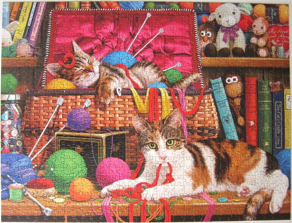 Two cats in a cozy craft room filled with yarn, books, and knitting supplies.