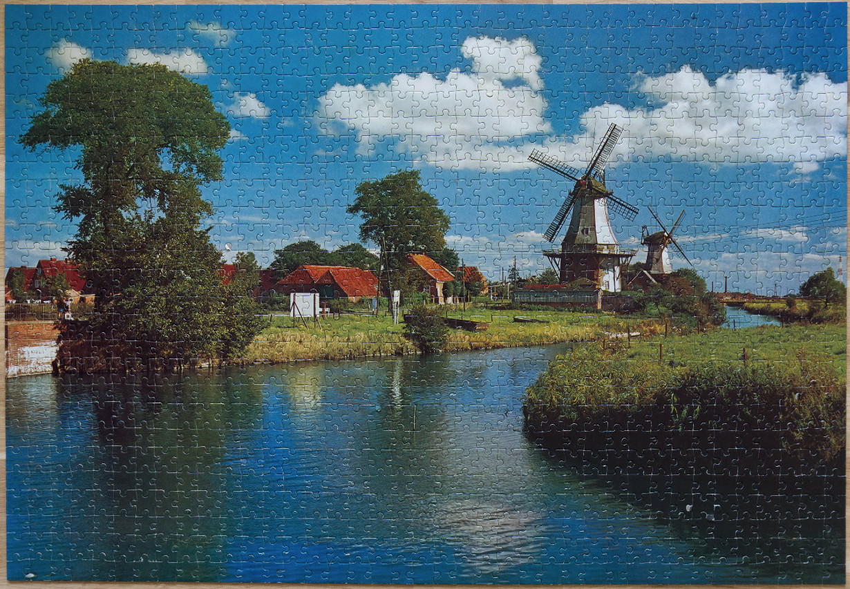 A scenic Dutch landscape featuring a winding canal, historic windmills, and traditional brick houses under a blue sky.