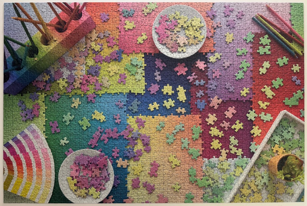 A colorful, vibrant tabletop scene featuring rainbow gradients, scattered shapes, and art supplies.