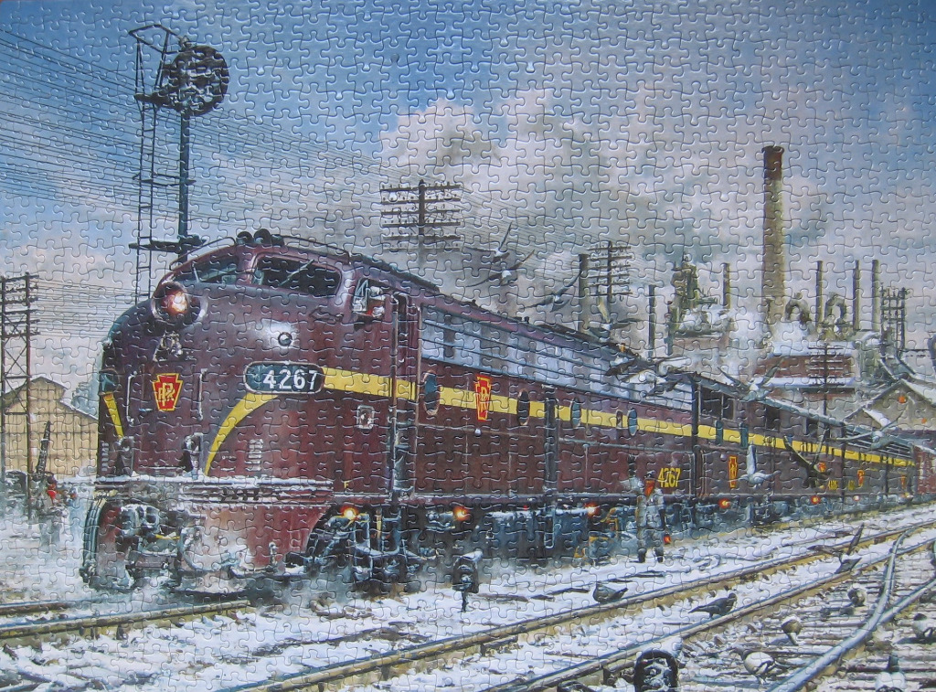 A vintage diesel locomotive pulling into a snowy industrial rail yard under a cloudy sky.