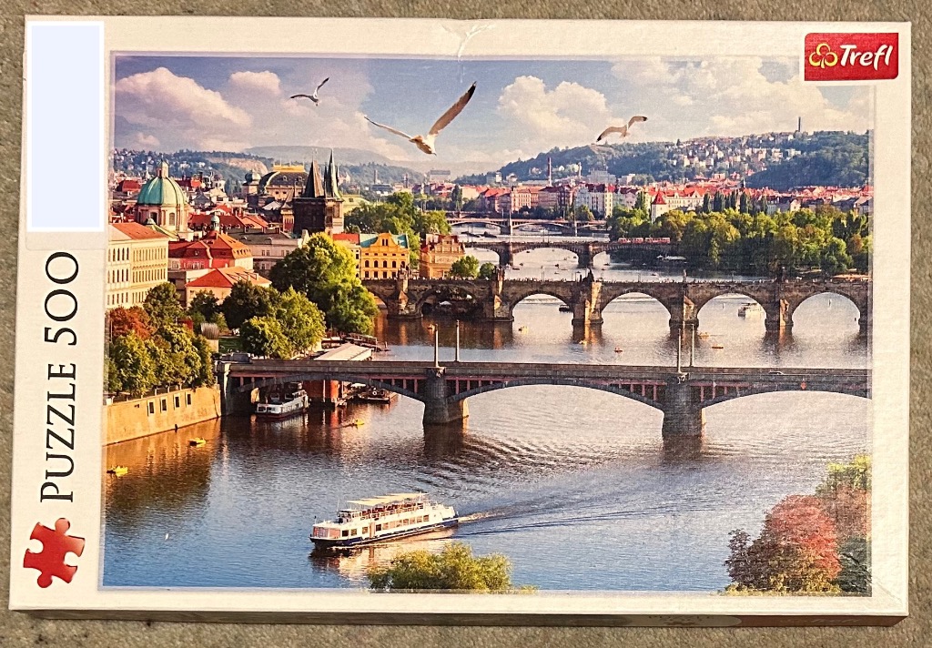 Panoramic view of the Vltava River in Prague with the Charles Bridge and historic cityscape under a sunny sky.