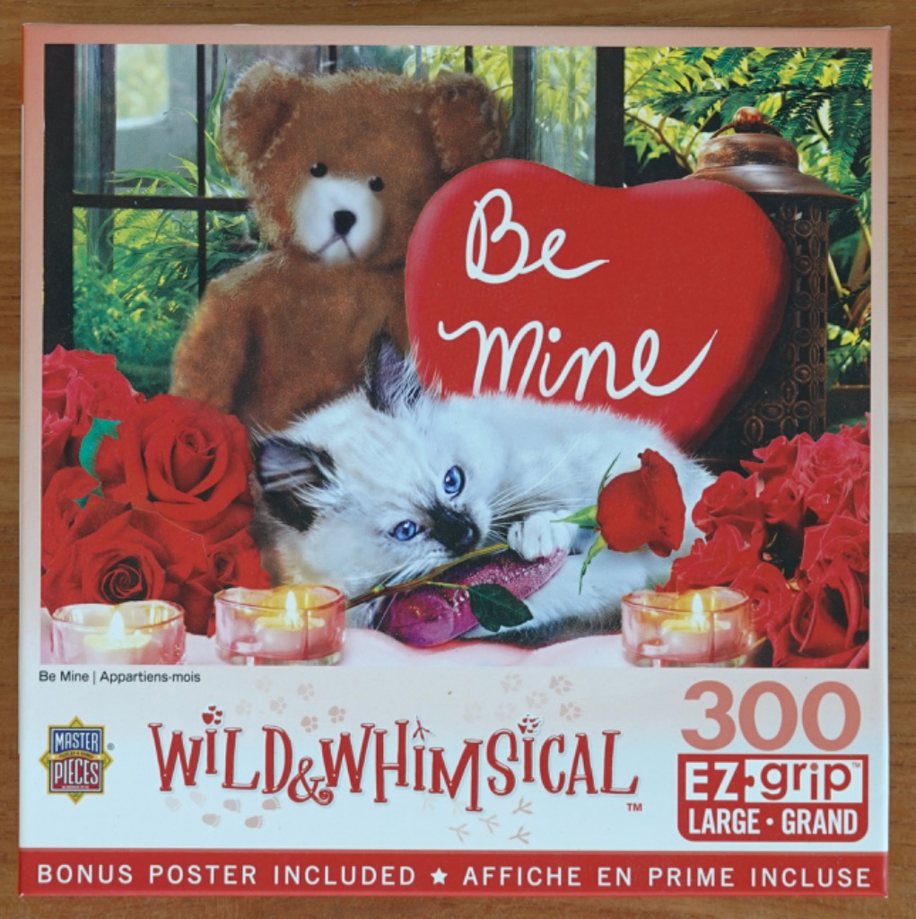 A fluffy kitten and a teddy bear sitting together with red roses and a heart shaped sign that says Be Mine.