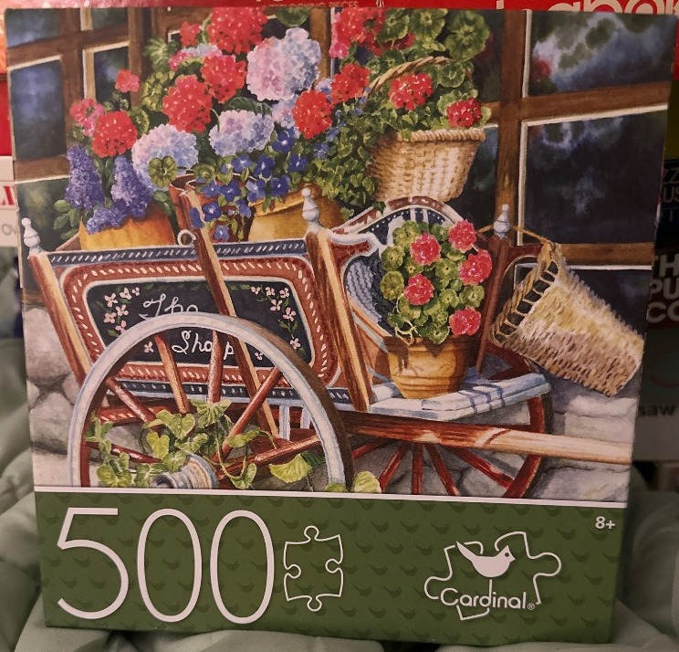 Decorative antique wooden cart overflowing with bright flowers in front of a rustic cottage window.