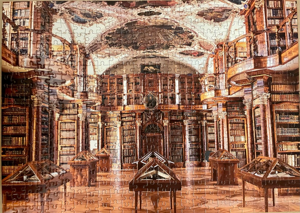 A photograph of a grand, multi-level baroque library interior with dark wood shelves and ornate ceiling frescoes.