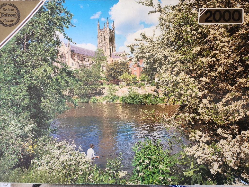 A lone fisherman by a river with a grand Gothic cathedral in the background, framed by flowering trees.