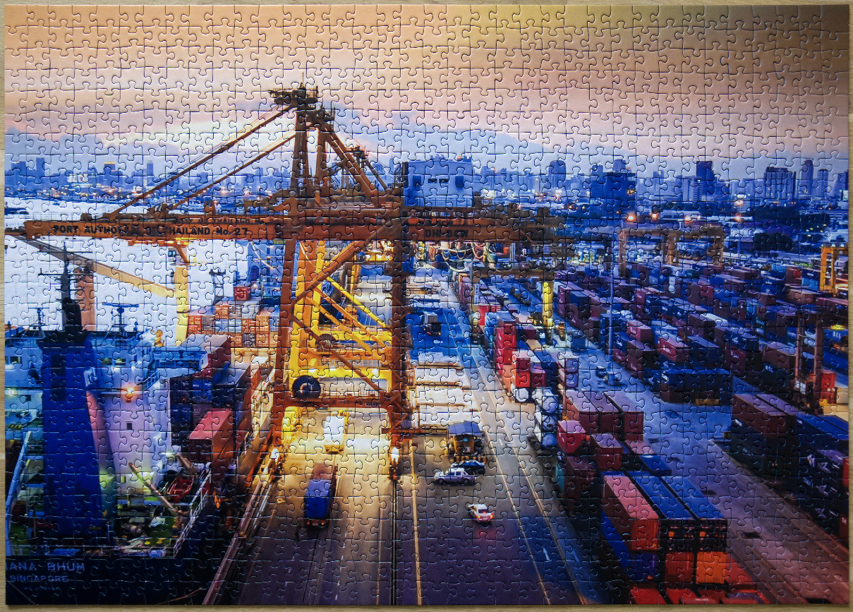 A sprawling shipping port at sunset with a large yellow gantry crane and stacks of colorful containers.