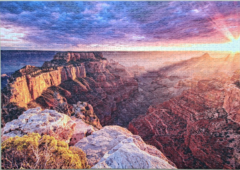 A panoramic photograph of the Grand Canyon at sunset with golden light and a purple, cloudy sky.