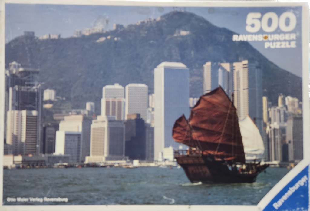 A traditional Chinese junk boat sailing in front of the Hong Kong skyline with Victoria Peak in the background.