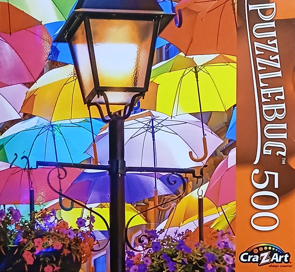 A street lamp illuminated against a sky filled with a dense canopy of colorful open umbrellas.