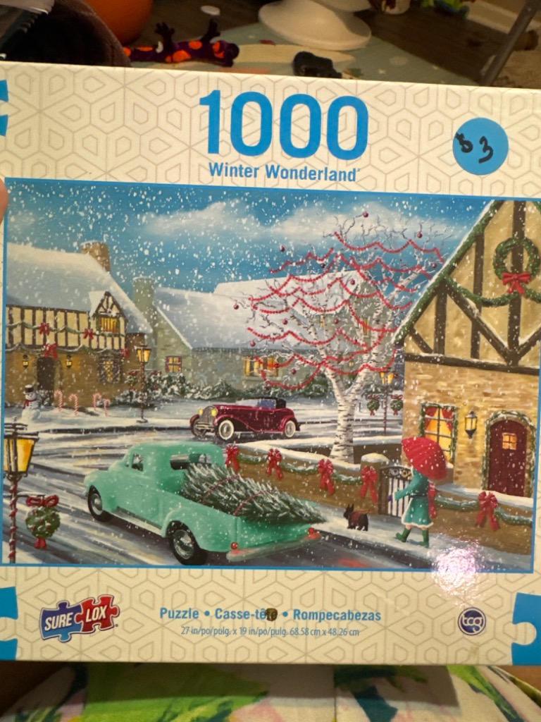 A nostalgic winter village scene with a vintage teal pickup truck carrying a Christmas tree down a snowy street.