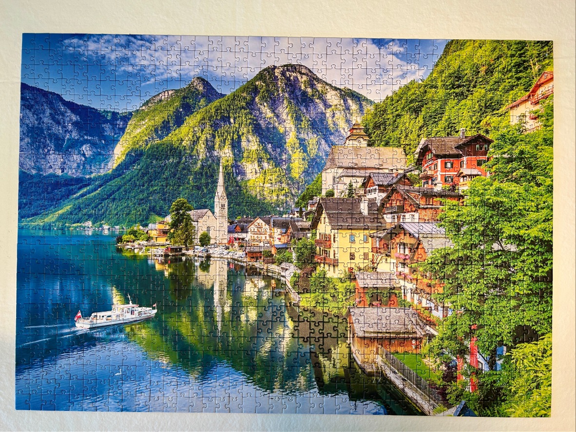 A scenic view of Hallstatt, Austria, featuring lakeside houses, a church spire, and mountains reflected in the water.