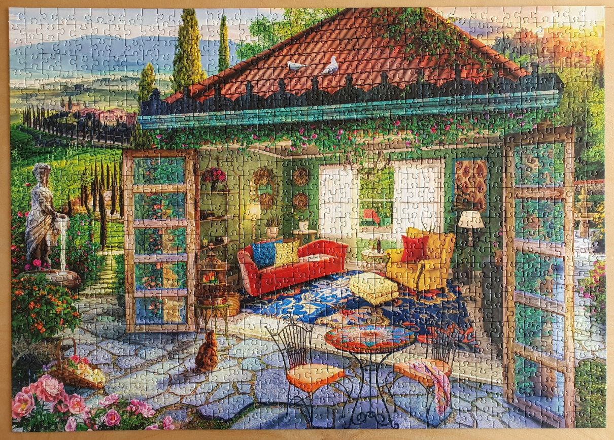 A cozy sunroom overlooking a Mediterranean landscape with a statue, garden, and interior lounge area.