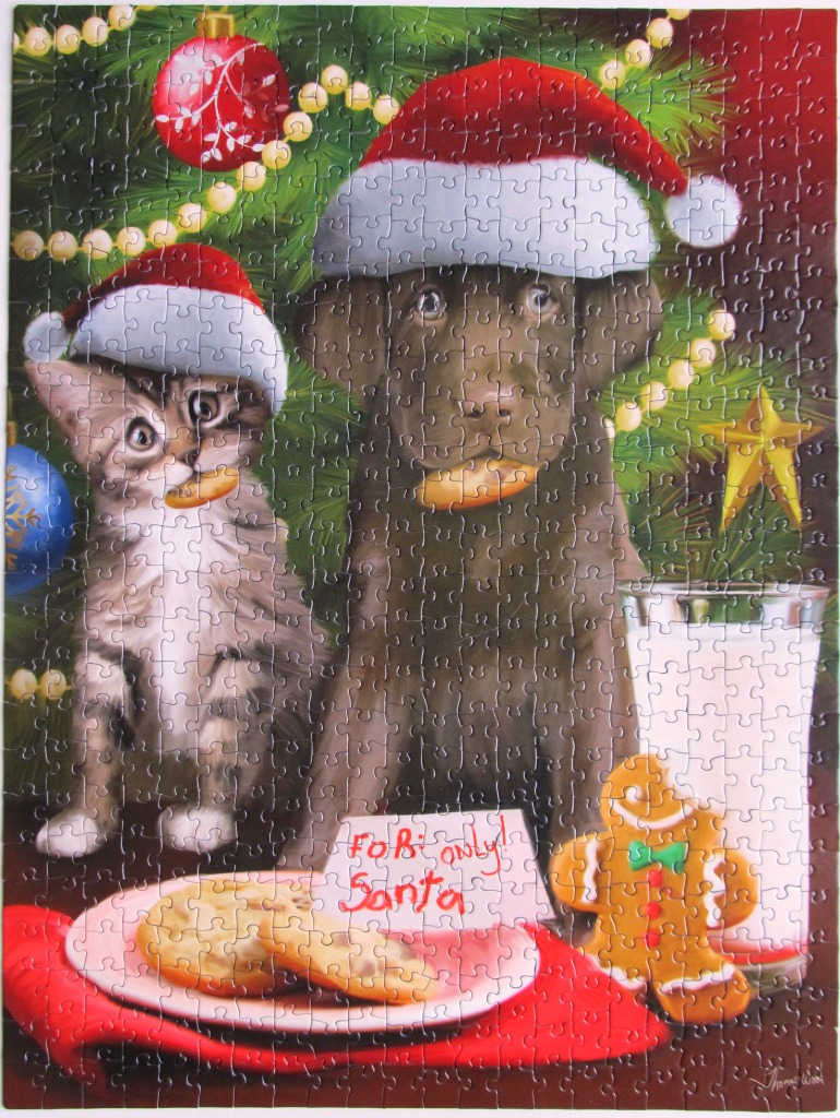 A chocolate Labrador and a tabby kitten wearing Santa hats in front of a Christmas tree with cookies and milk.