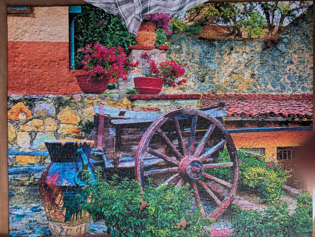 A rustic Mexican-style courtyard featuring a wooden wagon wheel, bright clay pots, and vibrant pink bougainvillea.