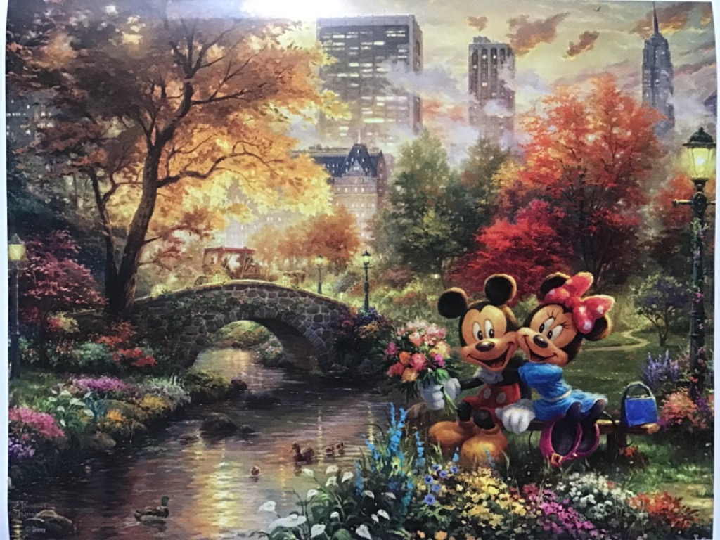 Mickey and Minnie Mouse sitting on a bench in a beautiful autumn park with a stream and city skyline.