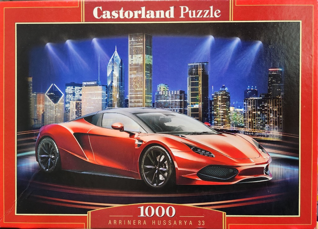 Red Arrinera Hussarya sports car parked in front of a brightly lit city skyline at night.