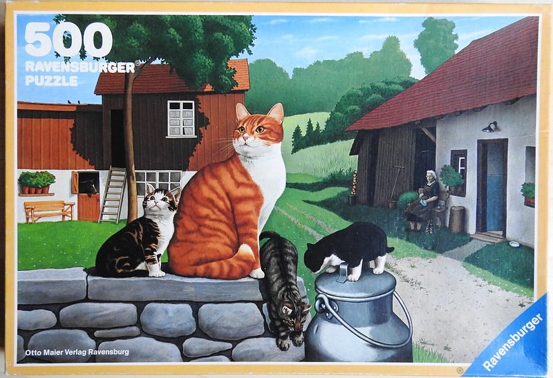 A group of cats near a farmhouse, including a large ginger cat on a stone wall and an elderly woman seated nearby.