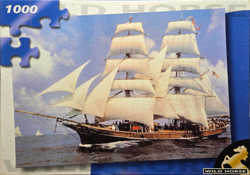 A majestic tall ship with white sails under a partly cloudy blue sky on the ocean.