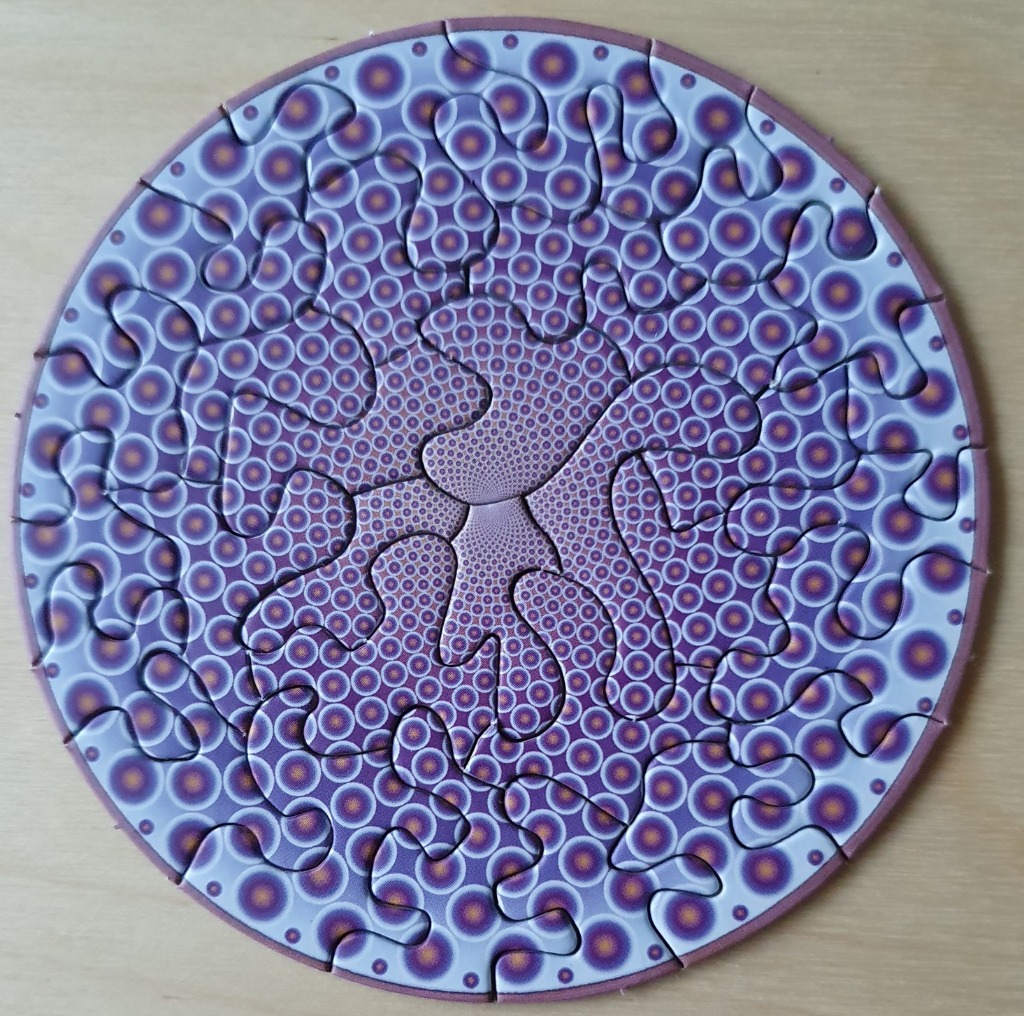 A circular fractal pattern featuring repetitive purple and orange concentric circles in a swirling, hypnotic design.