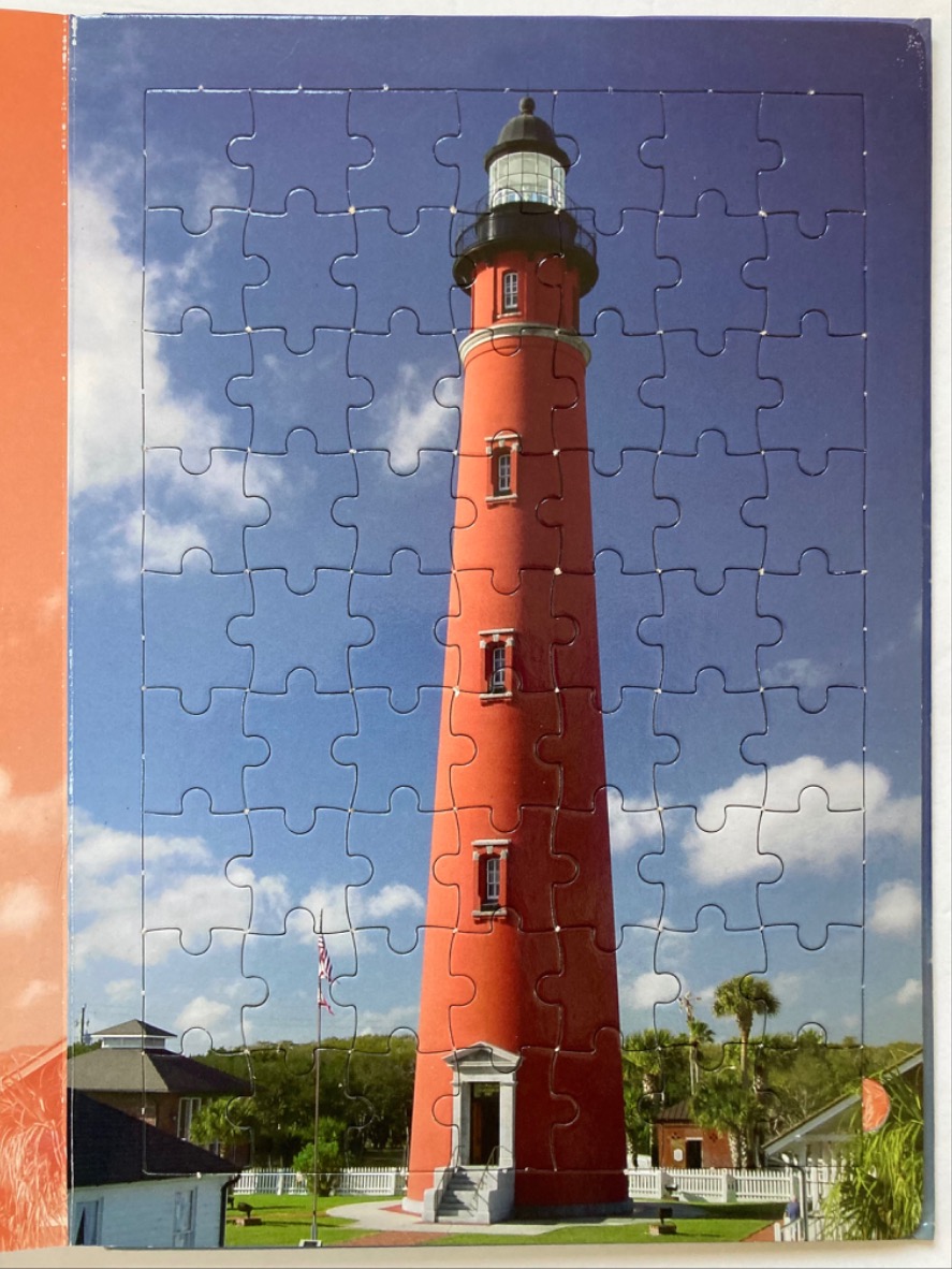 A tall, bright red lighthouse standing against a blue sky with scattered clouds.